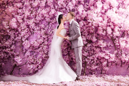 Creative purple flower wall at wedding, bride and groom kissins