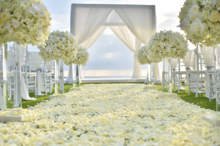 White wedding flowers positioned alongside the aisle and flower petals leading to the outdoor altar for wedding ceremony