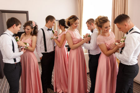 Bridesmaids wearing different pink dresses and pinning flowers on groomsmen