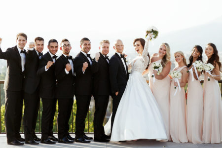 Bridal party in matching black tuxedos and long blush dresses next to bride and groom