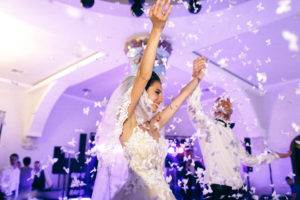 Bride and groom holding up hands under confetti