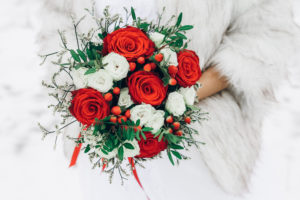 Bouquet of red roses with herbs and berries. Bouquet in the hands of the bride. Image with selective focus and toning.